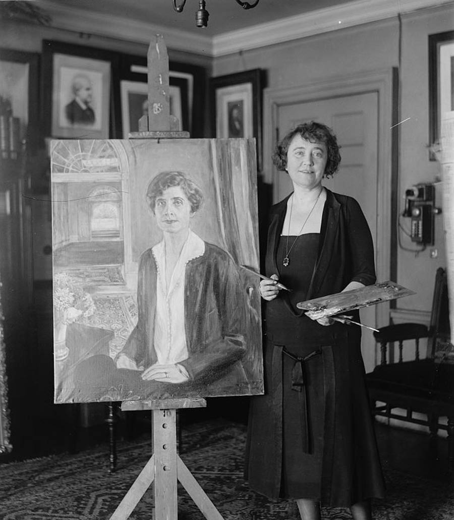 A photograph of Juliet Thompson standing next to her portrait of First Lady Grace Coolidge.