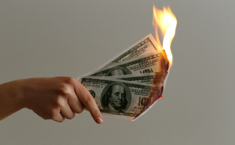 A hand holding burning bills of money, symbolizing the impermanence and fleeting nature of material wealth.