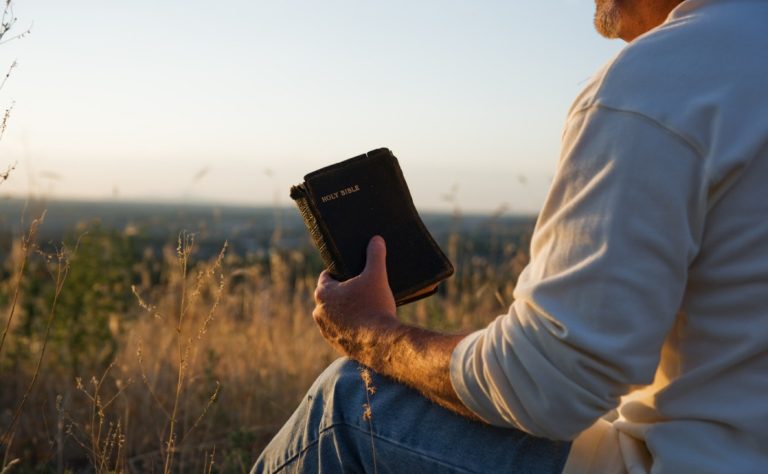 A person holding a Bible while gazing thoughtfully at the horizon, symbolizing reflection and spiritual contemplation.