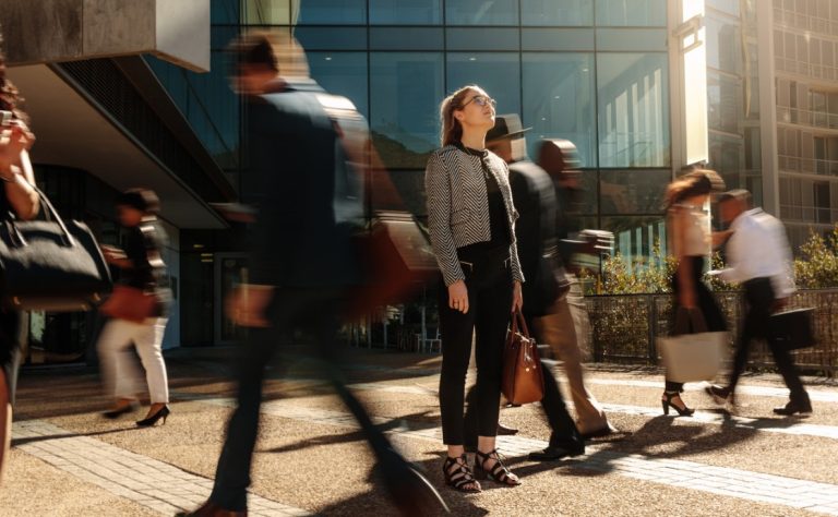 A woman standing still amidst a crowd of rushing people, gazing thoughtfully at the sky. What a Spiritual City Could Look Like